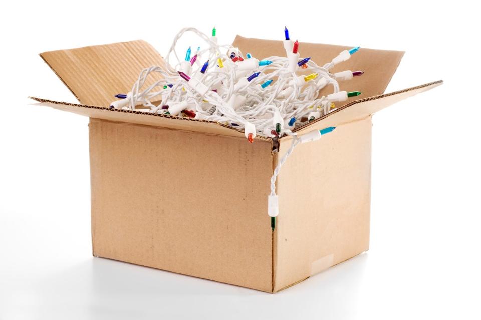 Cardboard box filled with Christmas lights on a white string.