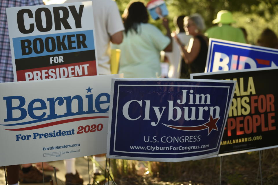 Supporters of many of the Democrats seeking their party's presidential nomination plant signs outside the venue for Majority Whip Jim Clyburn's "World Famous Fish Fry" on Friday, June 21, 2019, in Columbia, S.C. (AP Photo/Meg Kinnard)