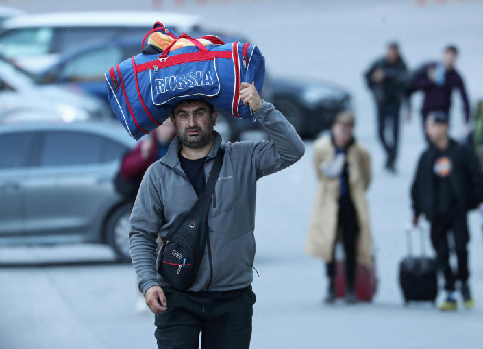 A man carries a duffel bag on his head and others wheel luggage as travelers from Russia cross the border into Georgia.