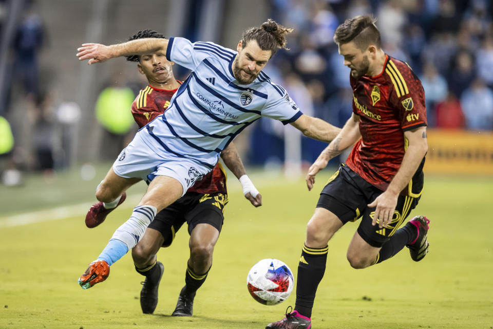Sporting Kansas City midfielder Graham Zusi, front left, attempts to step through the defense of Seattle Sounders midfielder Leo Chu, back left, and midfielder Kelyn Rowe, right, during the second half of an MLS soccer match on Saturday, March 25, 2023, in Kansas City, Kan. (AP Photo/Nick Tre. Smith)