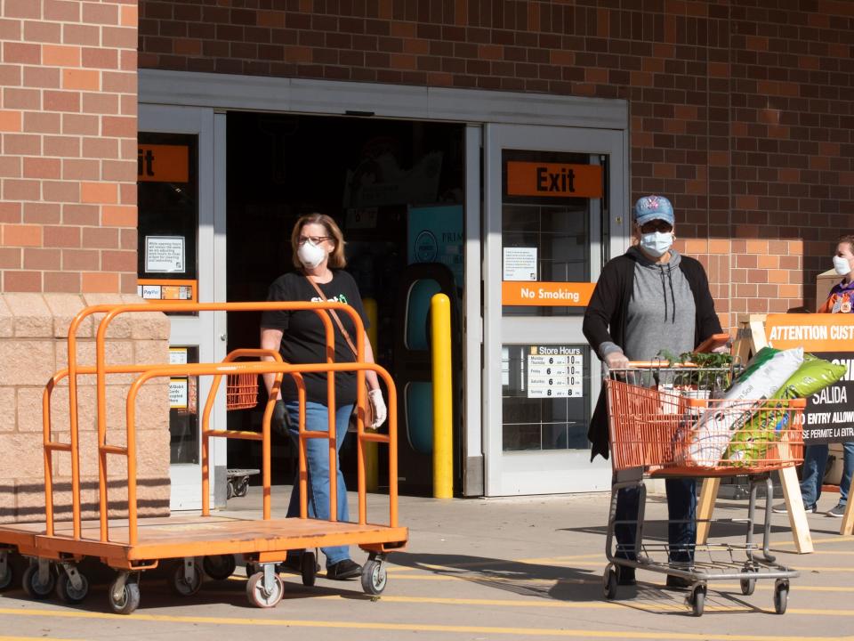 woman walking past a flatbed cart at home depot exit and another customer pushing a regular shopping cart
