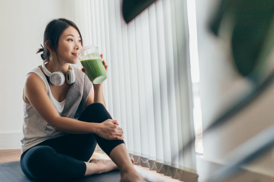 Young woman in sportswear drinking protein shake after exercise, relaxing at home.