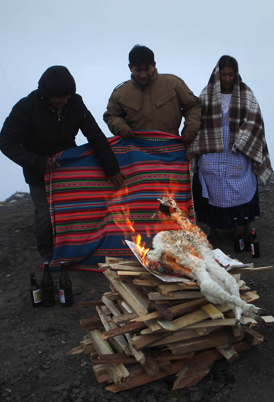 In this Aug. 15, 2012 photo, people burn a dead baby llama as an offering to the "Pachamama," or Mother Earth, on El Cumbre mountain, considered sacred, on the outskirts of La Paz, Bolivia.  During the month of August, people gather on sacred mountains to make offerings and ask for wealth to Mother Earth.  According to local agrarian tradition, Mother Earth awakes hungry and thirsty in August and needs offerings of food and drink in order for her to be fertile and yield abundant crops. (AP Photo/Juan Karita)