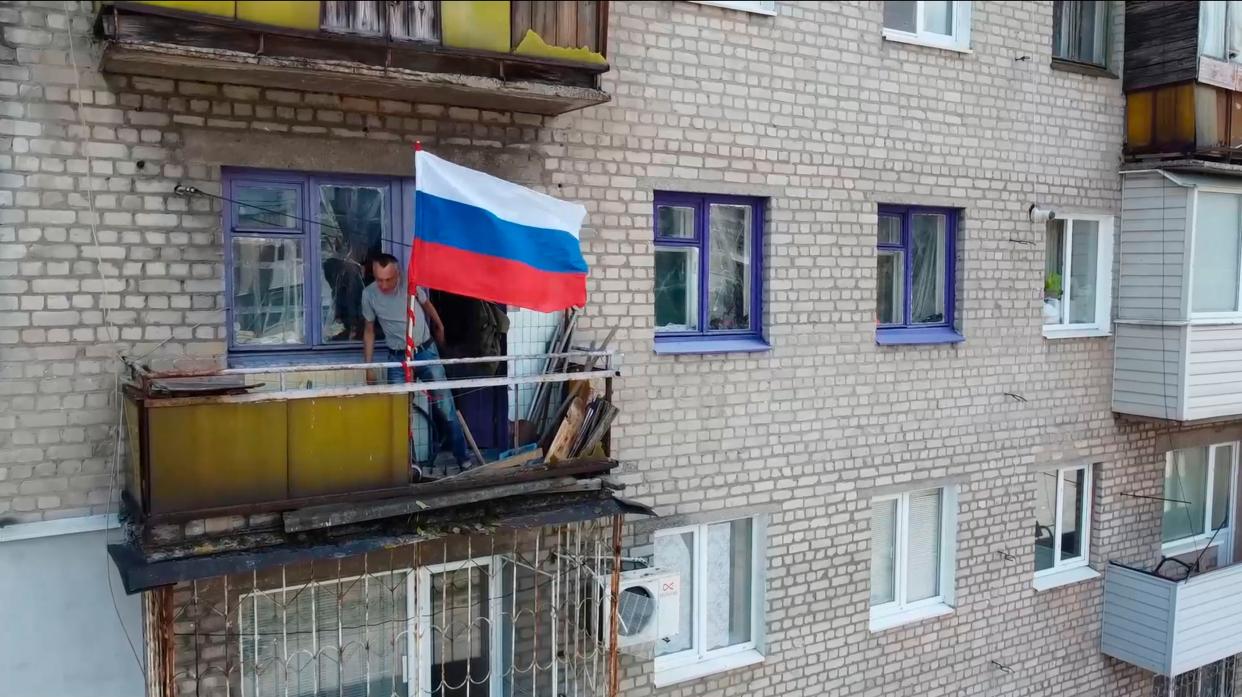 In this handout photo taken from video released by Russian Defense Ministry Press Service on Monday, July 4, 2022, a man sets a Russian national flag on a balcony of a residential building in Lysychansk, which is now territory under the Government of the Luhansk People's Republic control, eastern Ukraine.