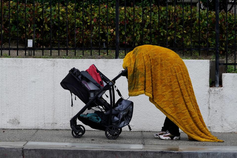 A homeless person shields themselves from the rain under a wet cover in downtown Los Angeles Tuesday, Dec. 14, 2021.
