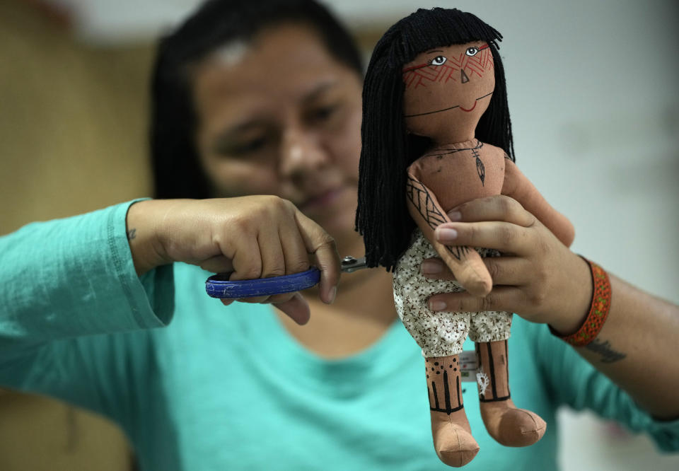 Atyna Pora, of Brazil's Anambe indigenous group, clips the hair made of yarn of an indigenous doll, at a sewing workshop in Rio de Janeiro, Brazil, Tuesday, May 24, 2022. Pora and her mother Luakam Anambe who make the dolls bearing faces and body paints of different Indigenous groups, have sold more than 5,000 of their dolls. (AP Photo/Silvia Izquierdo)