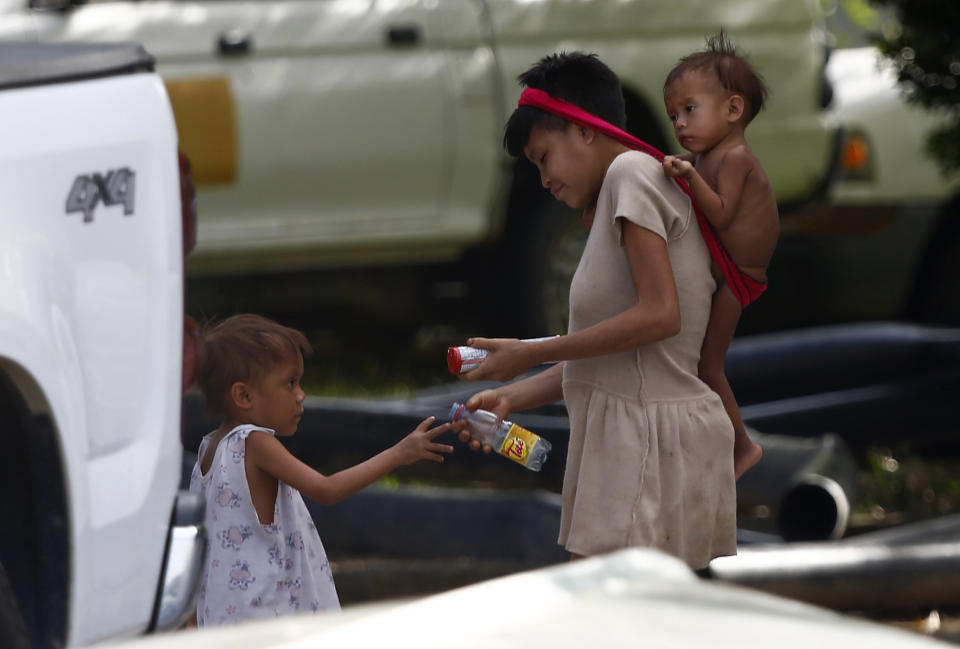 A Yanomami child hands cookies and an empty bottle to a Yanomami woman carrying a baby, on the grounds of the Saude Indigenous House, a center responsible for supporting and assisting Indigenous people in Boa Vista, Roraima state, Brazil, Wednesday, Jan. 25, 2023. The government has declared a public health emergency for the Yanomami people in the Amazon, who are suffering from malnutrition and diseases such as malaria. (AP Photo/Edmar Barros)