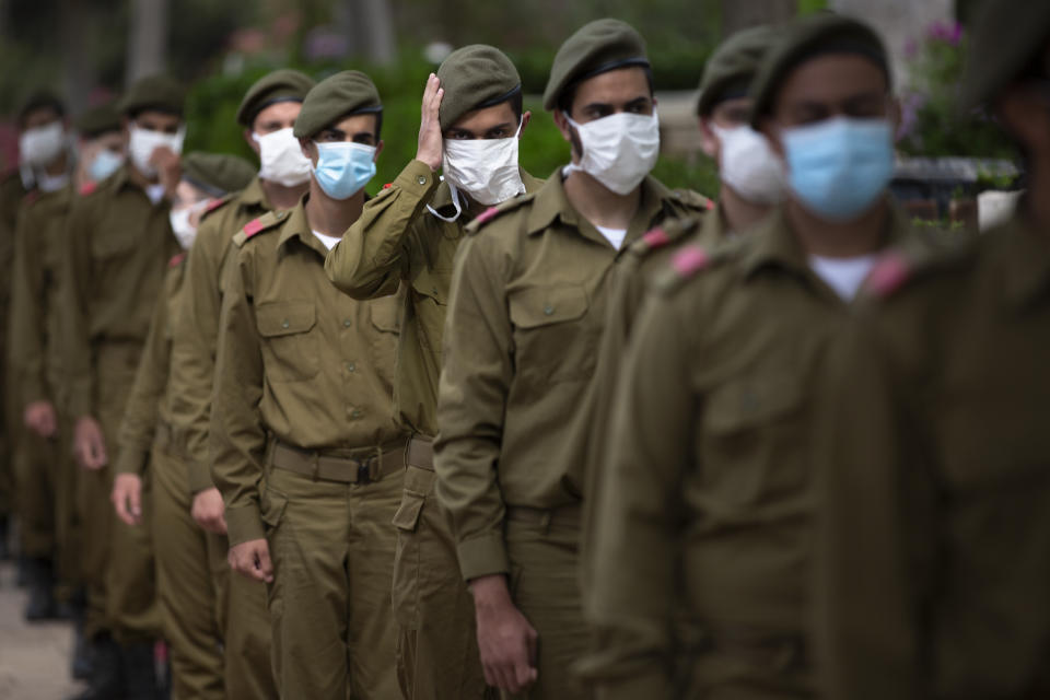 Israeli soldiers wearing protective face masks amid concerns over the country's coronavirus outbreak, stand next to graves of fallen soldiers on the eve of memorial Day in Kiryat Shaul Military Cemetery in Tel Aviv, Israel, Monday, April 27, 2020. This year the government had banned public memorial services at military cemeteries as part of its measures to help stop the spread of the virus. Israel marks the annual Memorial Day in remembrance of soldiers who died in the nation's conflicts, beginning at dusk Monday until Tuesday evening. (AP Photo/Oded Balilty)