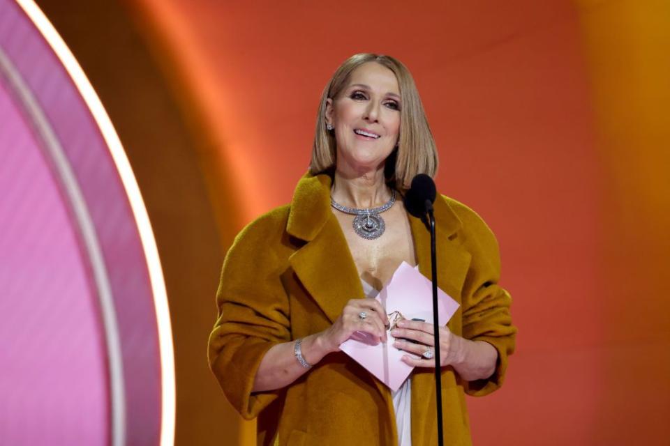 celine dion smiling and holding a pink envelope as she presents an award