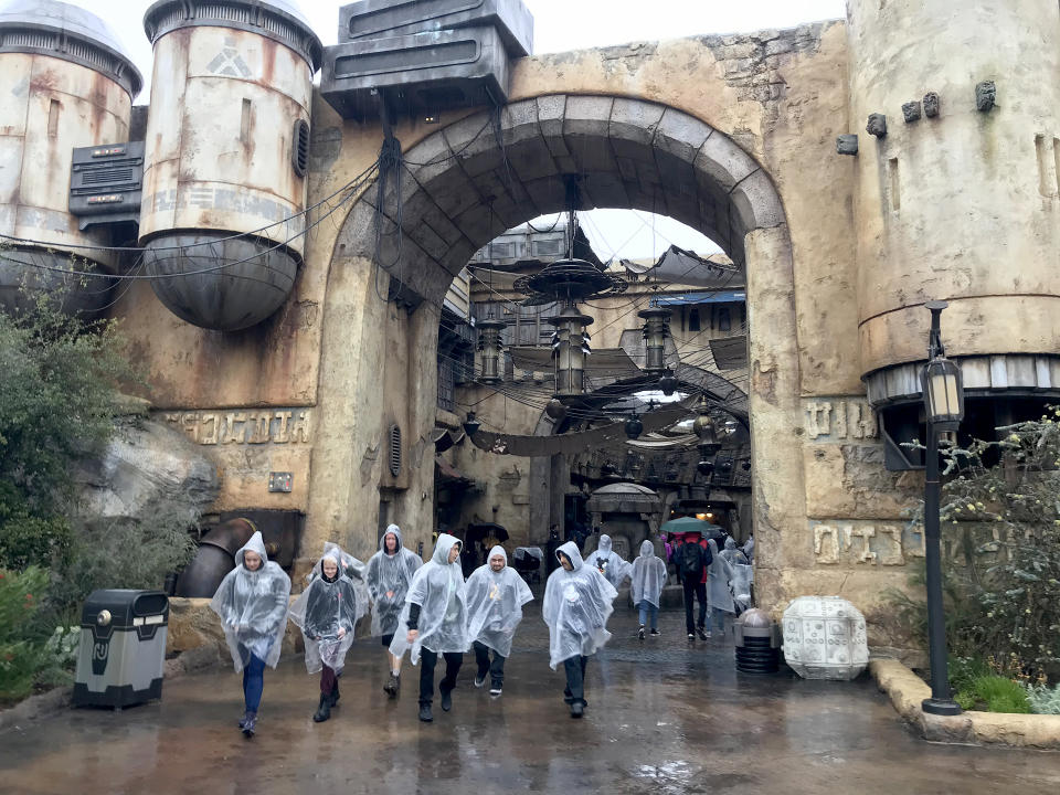 ANAHEIM, CA - MARCH 12:  Disneyland guests wearing ponchos walk past The Marketplace inside Star Wars: Galaxy's Edge in Disneyland amid rain showers in Anaheim, Calif., on March 12, 2020.  Disneyland will temporary close the Disneyland Resort and Disney California Adventure in Anaheim in response to the expanding threat posed by the Coronavirus Pandemic. The closure takes effect Saturday and lasts through the end of March. Disneyland and Disney California Adventure will close Saturday morning through the end of the month in response to Gov. Gavin Newsom and state health officials recommendation that gatherings of 250 or more people be canceled across the state, company officials said. (Photo by Allen J. Schaben / Los Angeles Times via Getty Images)