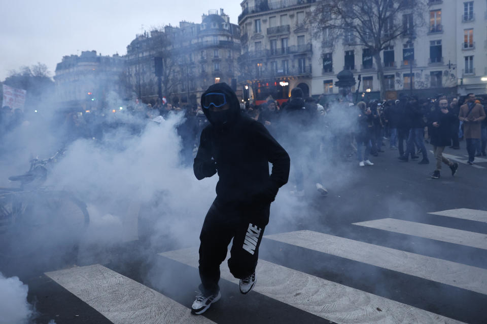 Youth runs away through tear gas during a demonstration against pension changes, Thursday, Jan. 19, 2023 in Paris. Workers in many French cities took to the streets Thursday to reject proposed pension changes that would push back the retirement age, amid a day of nationwide strikes and protests seen as a major test for Emmanuel Macron and his presidency. (AP Photo/Lewis Joly)