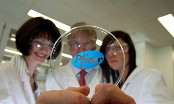 Three scientists holding a glass circle with the Pfizer logo on it.