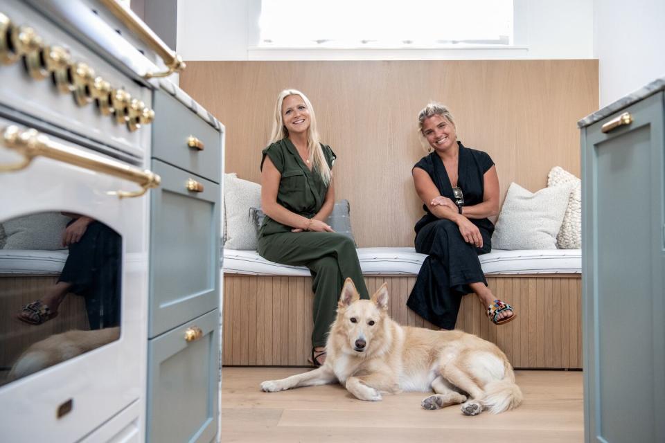 Two women sit on a banquette with a dog at their feet.