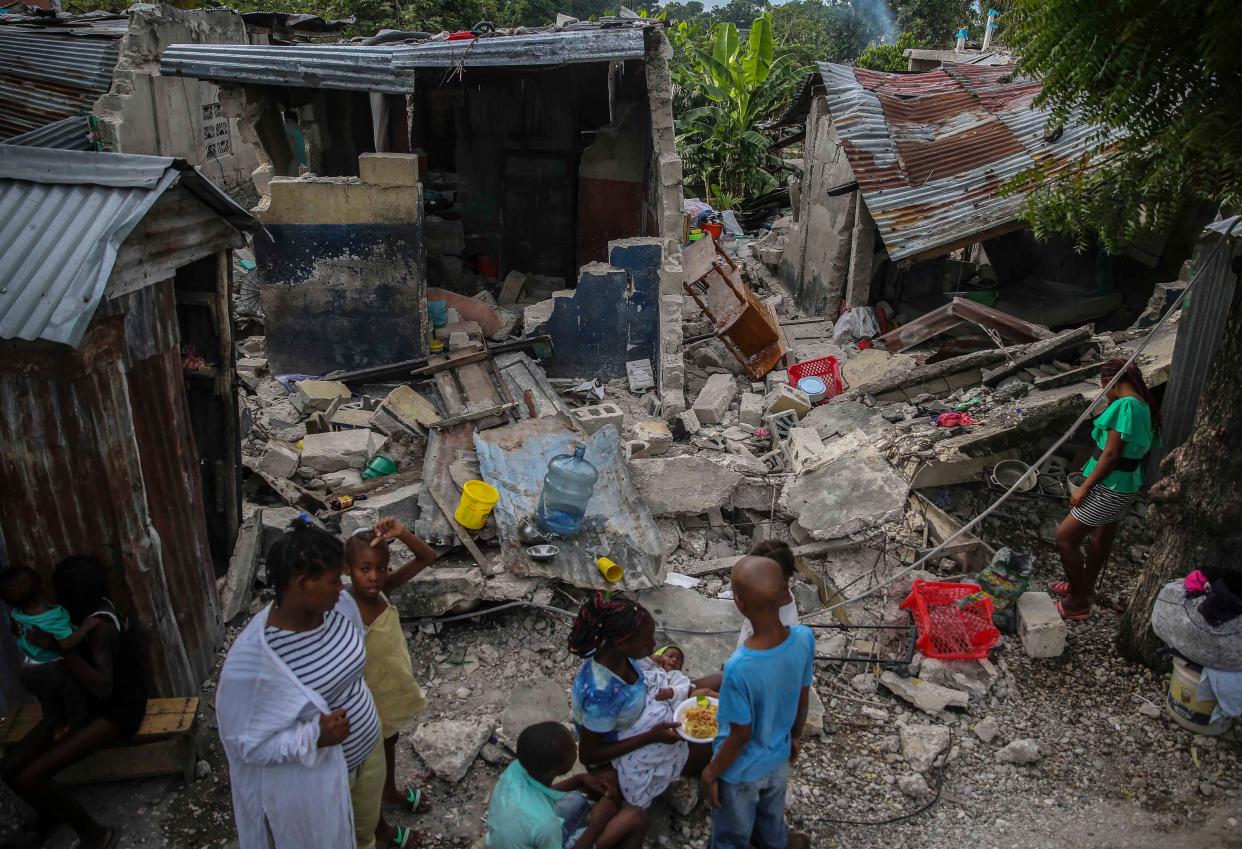 A family eats breakfast in front of homes destroyed by a 7.2 magnitude earthquake in Les Cayes, Haiti on Sunday, Aug. 15, 2021.