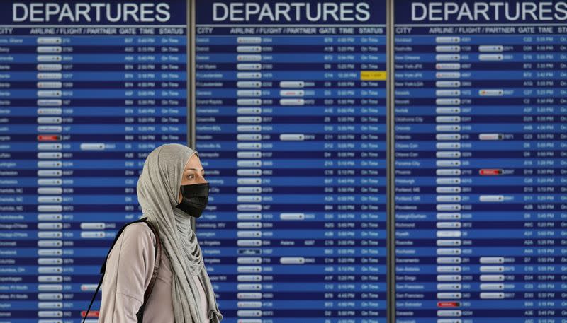 FILE PHOTO: A woman passes a departure board at Dulles International Airport in Virginia