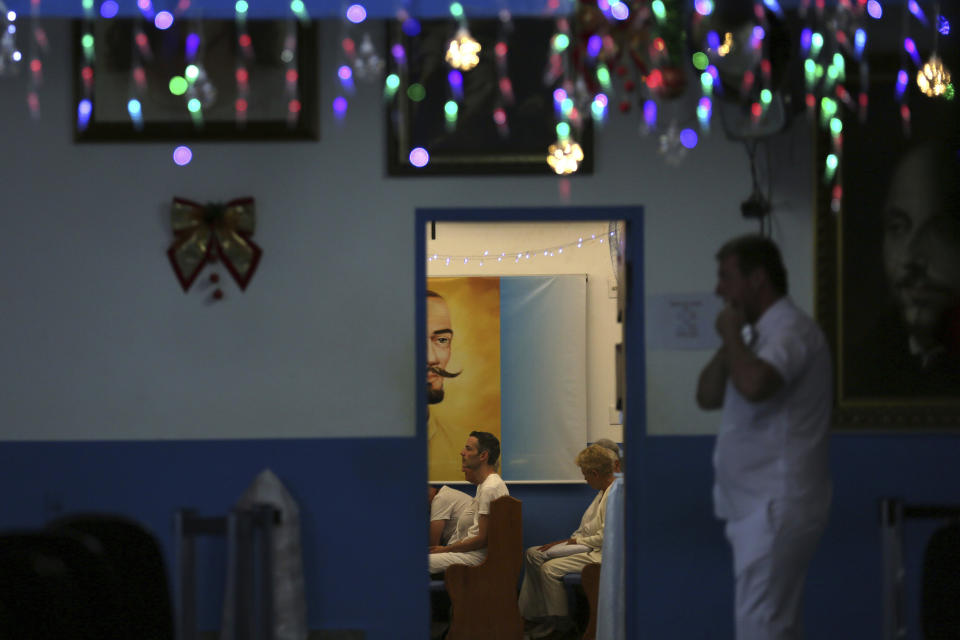 In this Jan. 4, 2019 photo, people sit inside a healing room decorated with images of Jesus Christ and spiritual healer Joao Teixeira de Faria, at the Casa de Dom Inacio, in Abadiania, Brazil. It is here that de Faria, who over the decades came under sharp scrutiny from critics who deemed him a charlatan, performed "psychic" surgeries that could heal a wide range of maladies. (AP Photo/Eraldo Peres)