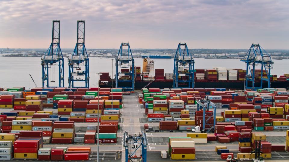 Aerial shot of the Port of Baltimore at sunset, looking across and intermodal container yard towards a ship being unloaded by cranes.