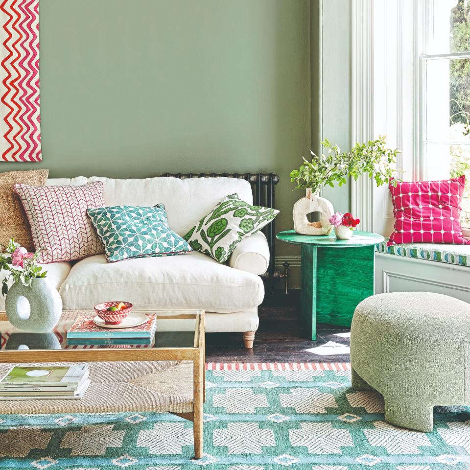 A sage green-painted living room with a cream sofa and a pouffe matching the walls