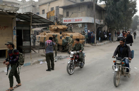 Men ride motorcycles as Turkish soldiers are seen with their military vehicle in the center of Afrin, Syria March 24, 2018. REUTERS/Khalil Ashawi