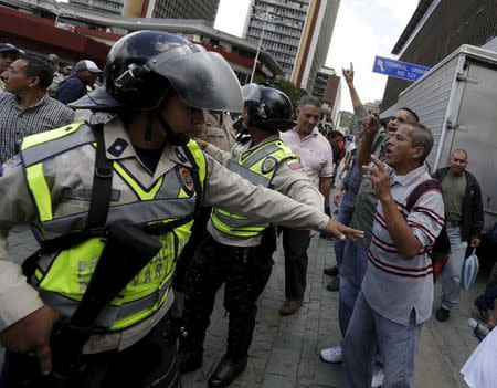 A police officer blocks supporters of Venezuela's President Nicolas Maduro (R) from passing after Lilian Tintori, wife of jailed Venezuelan opposition leader Leopoldo Lopez, delivered a letter demanding that the government set a date for this year's parliamentary elections, outside the National Electoral Council (CNE) offices in Caracas, June 16, 2015. REUTERS/Jorge Dan Lopez