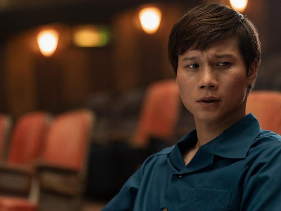 hoa xuande as the captain in the sympathizer. he's a young man with dark hair, looking skeptically to the side while wearing a blue shirt and sitting in the seats of a theater