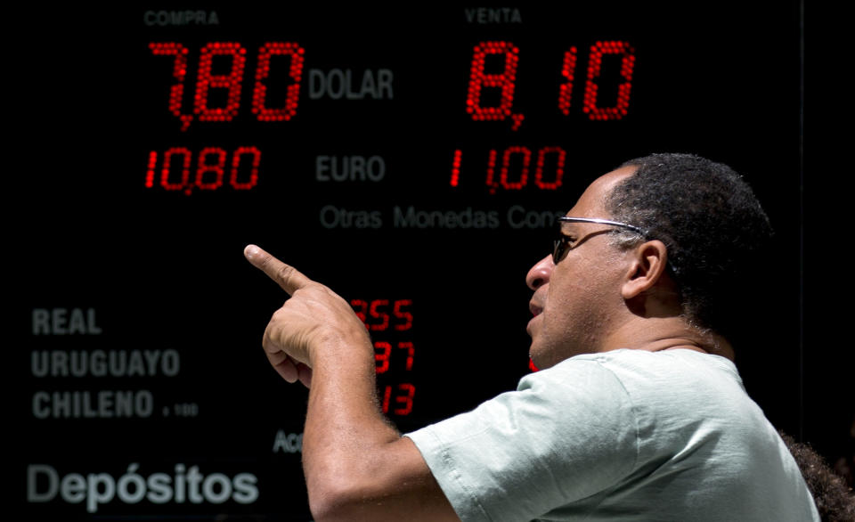 A man points forward as he passes in front of a board displaying going rates of U.S. dollars at a foreign exchange business in Buenos Aires, Argentina, Monday, Jan. 27, 2014. The Argentine government announced Friday it was relaxing restrictions on the purchase of U.S. dollars. The measure would start taking effect Monday, allowing Argentines to buy pesos for personal savings, reversing a 2012 restriction. (AP Photo/Natacha Pisarenko)