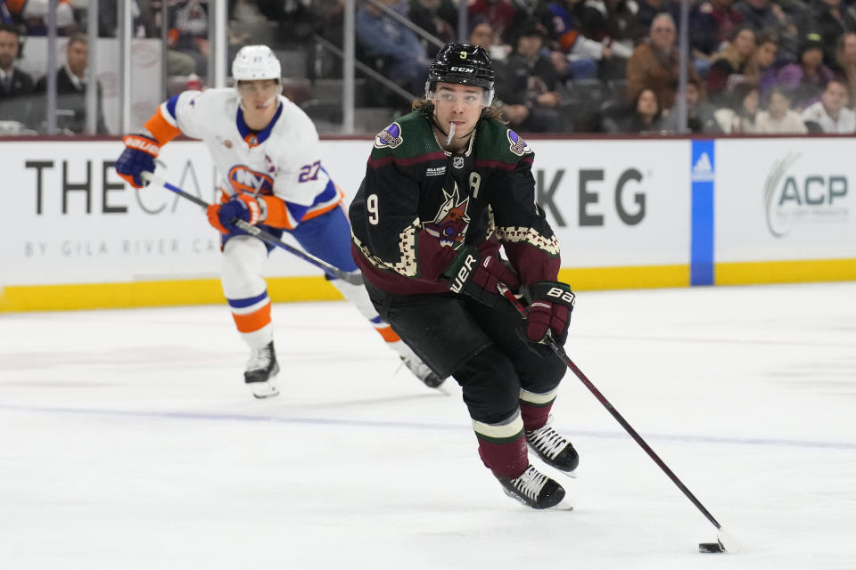 Arizona Coyotes right wing Clayton Keller (9) carries the puck towards the goal past New York Islanders left wing Anders Lee in the third period during an NHL hockey game, Friday, Dec. 16, 2022, in Tempe, Ariz. Arizona won 5-4. (AP Photo/Rick Scuteri)