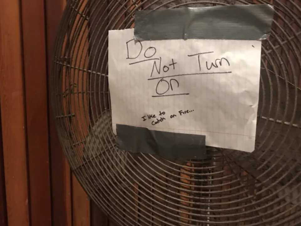 A giant oscillating fan has a sign on it that says "do not turn on, I like to catch on fire"