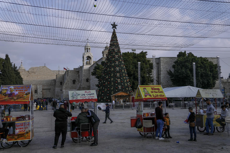 Palestinian vendors wait for clients next to the Christmas tree in Manger Square, adjacent to the Church of the Nativity, traditionally believed by Christians to be the birthplace of Jesus Christ, ahead of Christmas, in the West Bank city of Bethlehem, Monday, Dec. 5, 2022. Business in Bethlehem is looking up this Christmas as the traditional birthplace of Jesus recovers from a two-year downturn during the coronavirus pandemic. Streets are already bustling with visitors, stores and hotels are fully booked and a recent jump in Israeli-Palestinian fighting appears to be having little effect on the vital tourism industry. (AP Photo/ Mahmoud Illean)