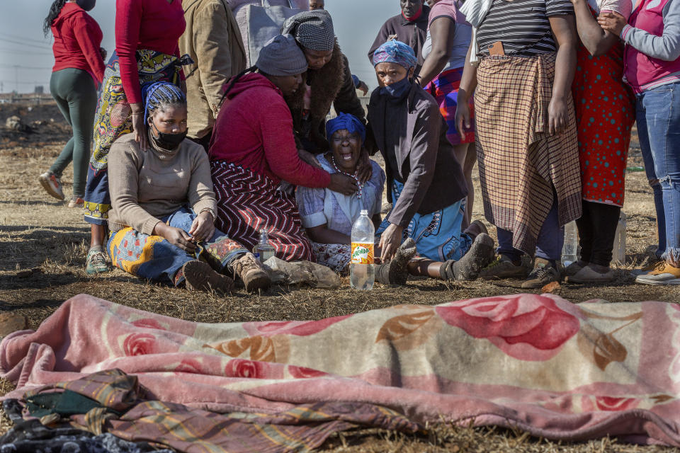 Family members mourn next to the body of a fifteen-year old boy who was allegedly shot dead by taxi association members attempting to disperse looters in Vosloorus, Johannesburg, Wednesday, July 14, 2021. Rioting has continued in parts of South Africa, in unrest sparked by the imprisonment last week of ex-President Jacob Zuma that has spiralled into days of looting in two of the country's nine provinces. (AP Photo/Yeshiel Panchia)