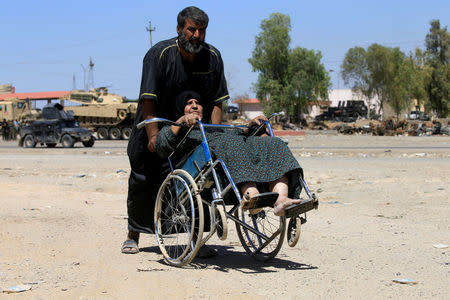 A displaced Iraqi man pushes a woman in a wheelchair during the battle between Iraqi forces and Islamic State militants in western of Mosul, Iraq, May 17, 2017. REUTERS/ Alaa Al-Marjani