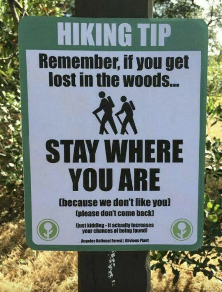 Panneau avec un conseil de randonnée conseillant de rester sur place en cas de perte dans les bois pour de meilleures chances d'être retrouvé, avec une remarque ludique