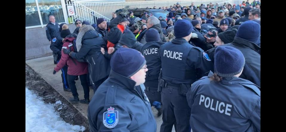 This screen shot from a CBC cellphone video captures the seconds before Richard Martin (wearing a black baseball hat with orange trim, with his face obscured by the bib of his hat) is taken to the ground during a protest in St. John's on the morning of March 20.