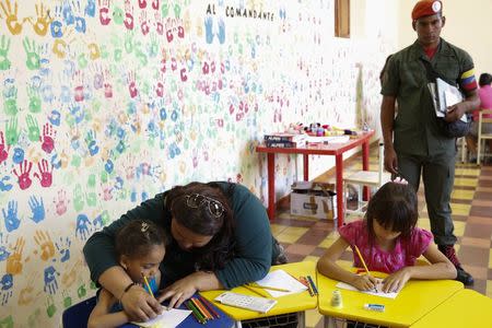 A woman helps a child with her drawing during a writing workshop at the 4F military fort in Caracas December 14, 2014. REUTERS/Carlos Garcia Rawlins