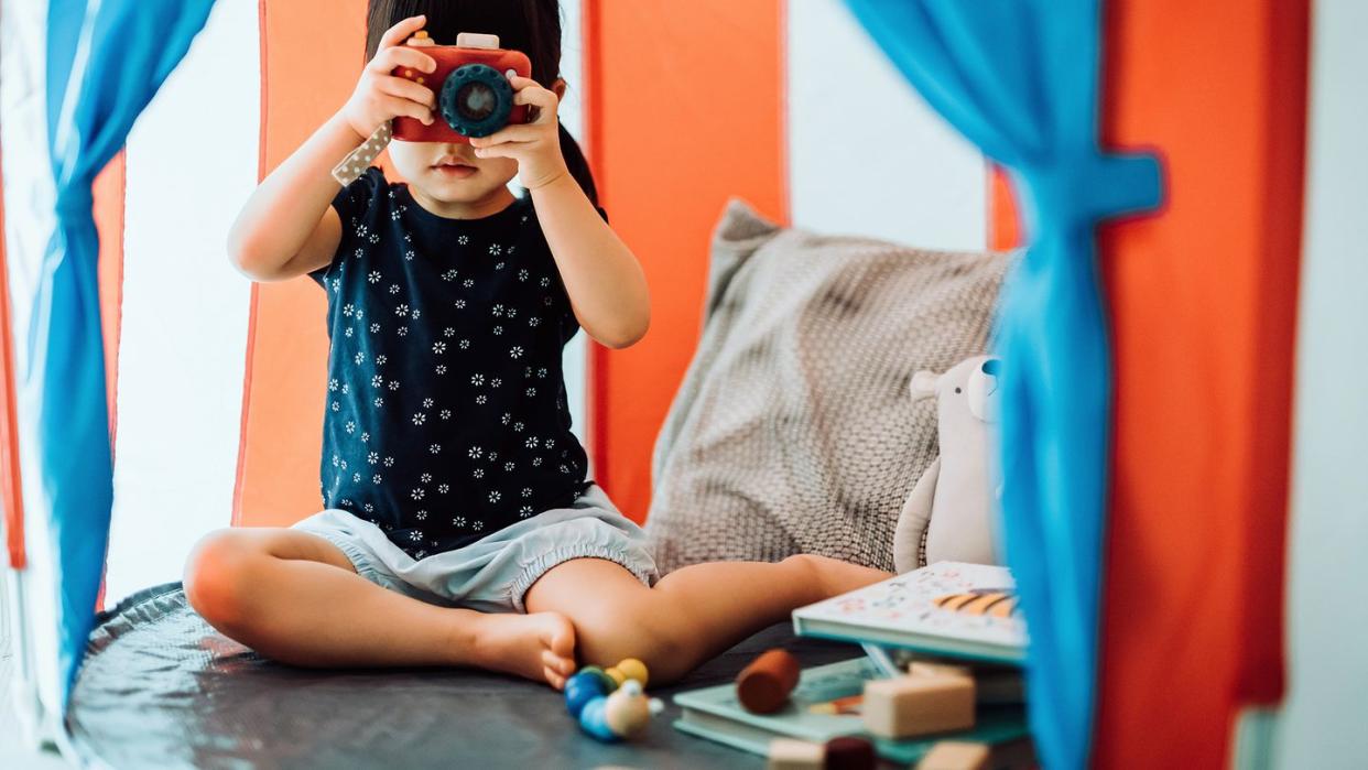 2 year old playing in play tent with camera blocks and books