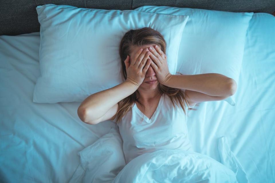 mujer sin poder dormir en la cama, tapándose los ojos con las manos