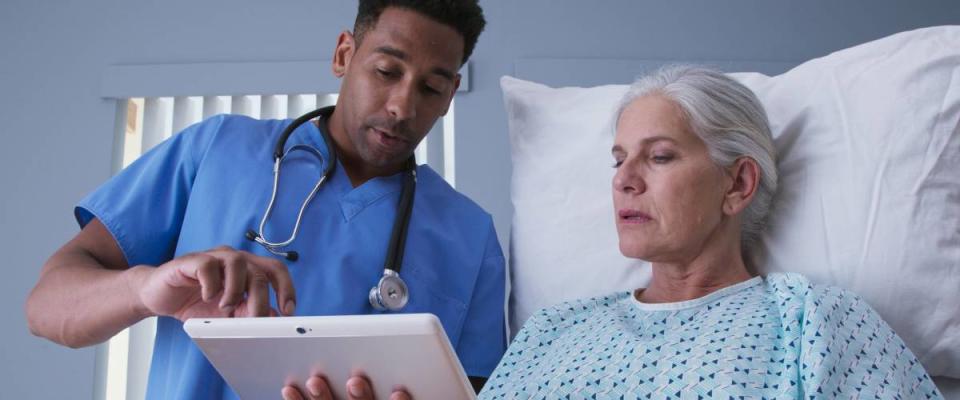 Male registered nurse showing ill elderly woman electronic pad