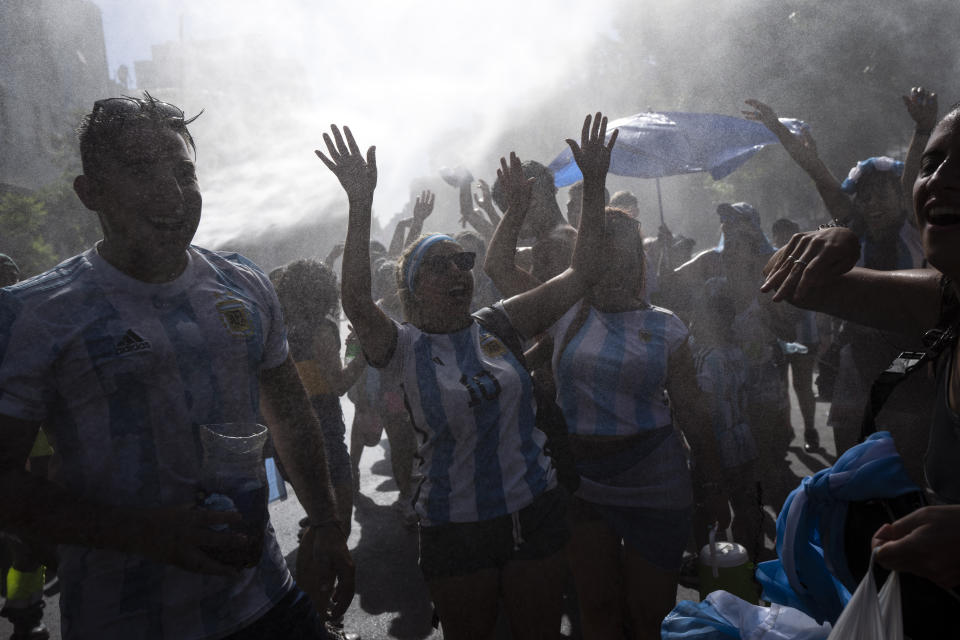 Soccer fans waiting for a homecoming parade for the players who won the World Cup title, are cooled off with water sprayed by municipal workers, in Buenos Aires, Argentina, Tuesday, Dec. 20, 2022. A parade to celebrate the Argentine World Cup champions was abruptly cut short Tuesday as millions of people poured onto thoroughfares, highways and overpasses in a chaotic attempt to catch a glimpse of the national team. (AP Photo/Rodrigo Abd)