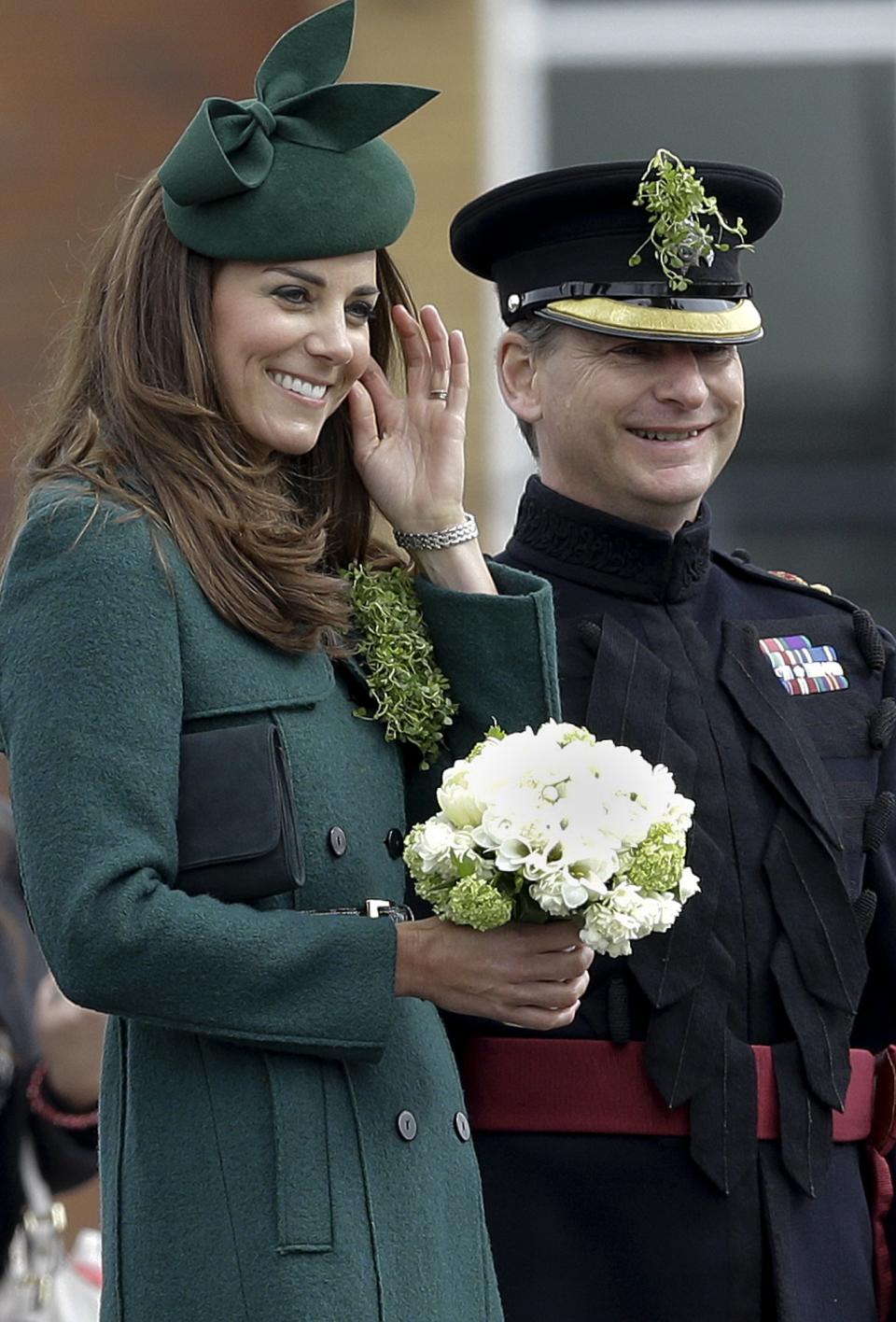 Kate, The Duchess of Cambridge smiles as she adjusts her hair during a visit to the 1st Battalion Irish Guards at the St. Patrick's Day Parade at Mons Barracks, Aldershot, in England, Monday, March 17, 2014. The Duke of Cambridge attended the Parade as Colonel of the Regiment. The Duchess of Cambridge presented the traditional sprigs of shamrocks to the Officers and Guardsmen of the Regiment. (AP Photo/Kirsty Wigglesworth)