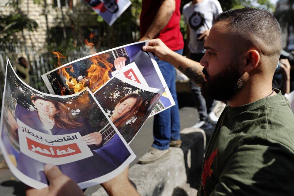 FILE - In this Thursday, Oct. 14, 2021 file photo, a supporter of the Shiite Hezbollah and Amal groups burns posters that show the U.S. Ambassador to Lebanon Dorothy Shea, and Arabic that reads: "Judge Bitar is the red line," during a protest against the judge who is investigating last year's deadly seaport blast, in front of the Justice Palace, in Beirut, Lebanon. For eight months Tarek Bitar, a relatively obscure judge has quietly investigated one of the world's worst non-nuclear explosions with only two assistants helping him -- and a lot of powerful detractors blocking him. For many Lebanese Bitar is their only hope for truth and accountability in a country that craves both. But for the country's entrenched political class, the 47-year-old Bitar has become a nightmare that needs to be dealt with. (AP Photo/Hussein Malla, File)