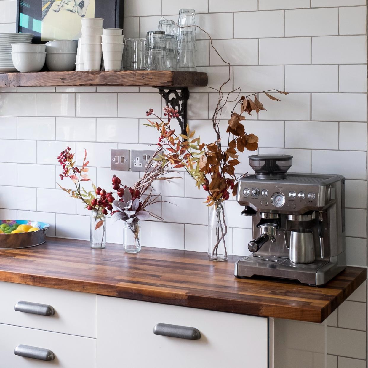  A white tiled kitchen with floral decor and a coffee machine. 