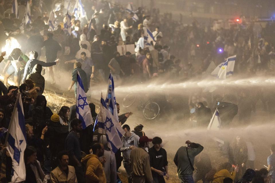 Israeli police use a water cannon to disperse demonstrators blocking a highway during a protest against plans by Prime Minister Benjamin Netanyahu's government to overhaul the judicial system in Tel Aviv, Israel, Monday, March 27, 2023. Tens of thousands of Israelis have poured into the streets across the country in a spontaneous outburst of anger after Prime Minister Benjamin Netanyahu abruptly fired his defense minister for challenging the Israeli leader's judicial overhaul plan. (AP Photo/Oren Ziv)