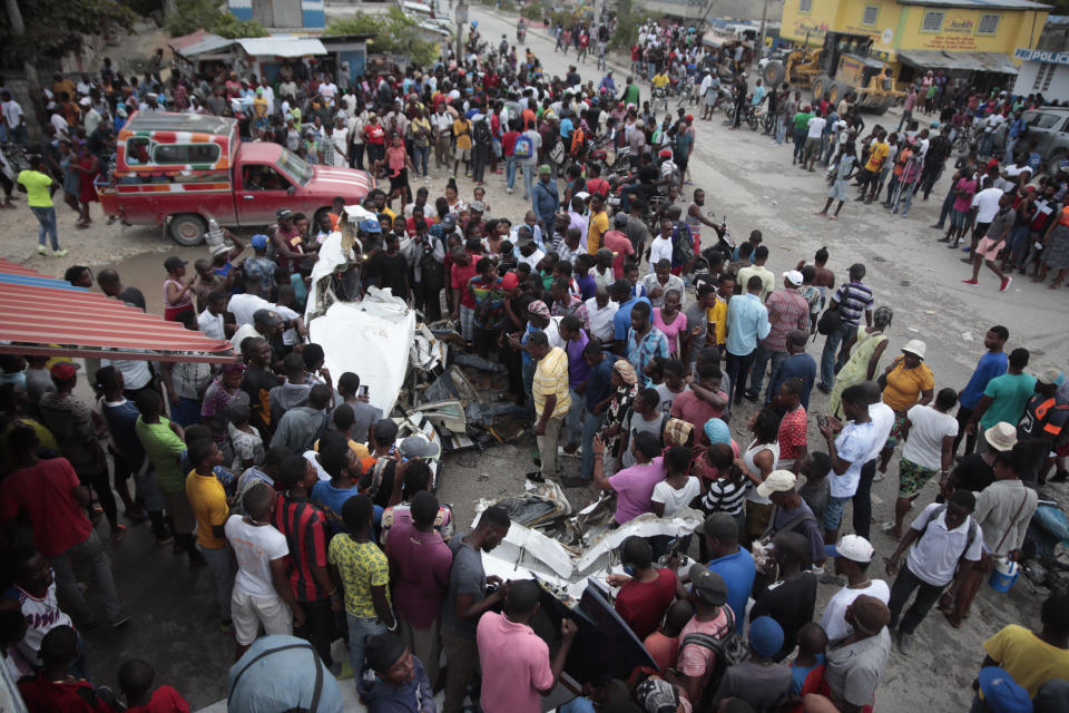 Onlookers mill around the crash site of a small plane in the community of Carrefour, Port-au-Prince, Haiti, Wednesday, April 20, 2022. Police report that the plane was headed to the southern coastal city of Jacmel when it tried to land in Carrefour, and that at least 5 people died in the accident. (AP Photo/Odelyn Joseph)