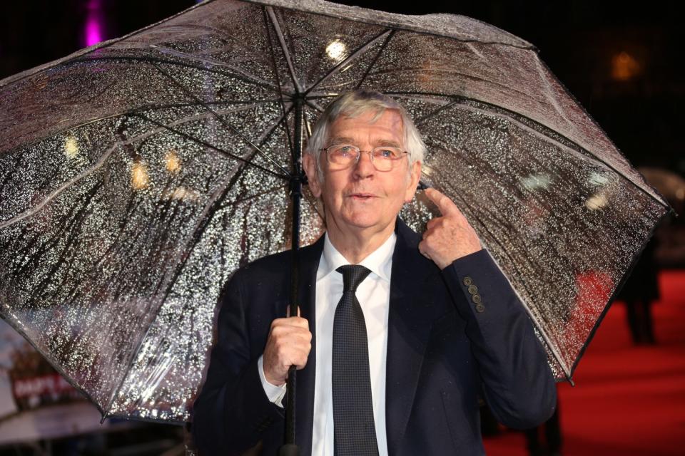 Actor Tom Courtenay stands in the rain under a clear umbrella