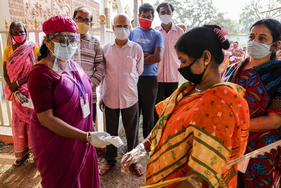 A woman takes the body temperature of a voter outside a polling booth during first phase of elections in West Bengal state in Medinipur, India, Saturday, March 27, 2021. Voting began Saturday in two key Indian states with sizeable minority Muslim populations posing a tough test for Prime Minister Narendra Modi’s popularity amid a months-long farmers’ protest and the economy plunging with millions of people losing jobs because of the coronavirus pandemic. (AP Photo/Bikas Das)