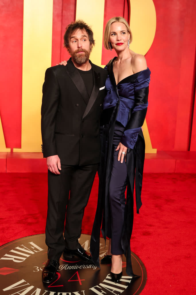 Two people posing, woman in off-shoulder gown with a train, man in a suit. Standing on an event mark with text "36th Anniversary."