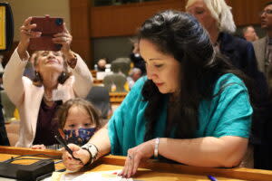  Rep. Linda Serrato (D-Santa Fe) signs into the official roster of state representatives as her daughter Alma watches on the first day of the 2023 Legislative Session. Serrato’s mother Rafaela Serrato is taking a picture with her phone. (Photo by Shaun Griswold / Source NM)