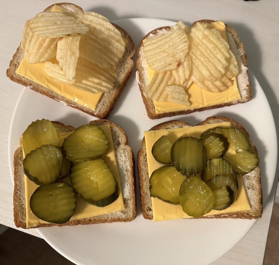 four slices of white bread with pickles and kraft singles on half and potato chips and more kraft singles on the other half