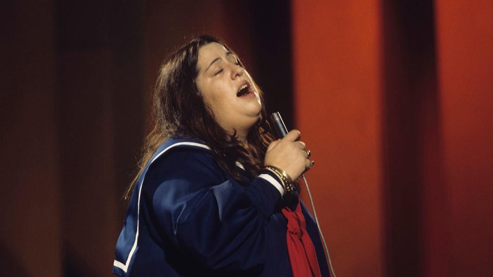 Mama Cass Elliot singing into a mic onstage