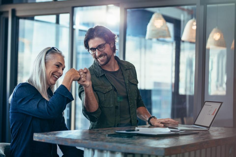 Two investors smile and touch fists in an office.